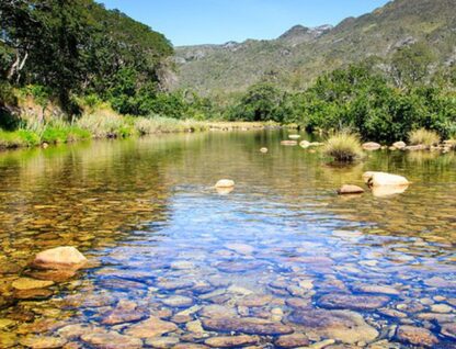 Imagem mostra Córrego do Mascate, com corpo d'água em primeiro plano e serra ao fundo