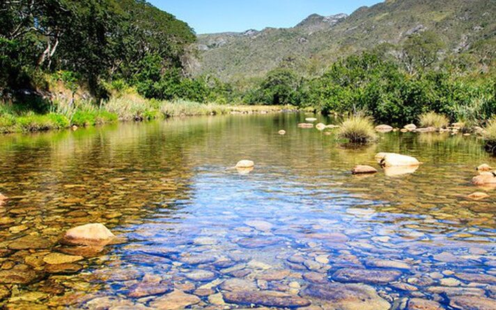 Imagem mostra Córrego do Mascate, com corpo d'água em primeiro plano e serra ao fundo