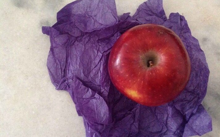 Imagem mostra uma maçã, vista de cima, em meio a papel roxo