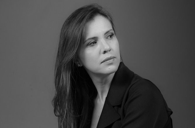 Foto em preto e branco. Carla Pedrosa, vestida com uma blazer preto, olha para o lado.