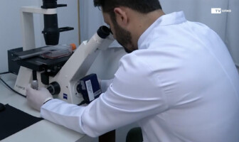 Pesquisador com jaleco olha pelas lentes de um microscópio