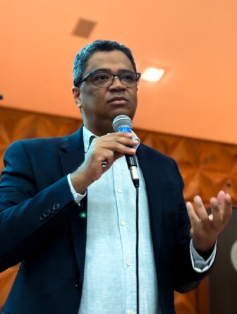 Helder, vestido de camisa azul clara e paletó azul marinho, segura microfone