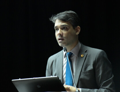 Hugo Valadares, de terno cinza e gravata azul, fala ao microfone