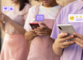 Três jovens, vestidos em tons de rosa e roxo, com celulares nas mãos. Sobre os aparelhos estão ícones de mensagem, coração, emoji e estrelas