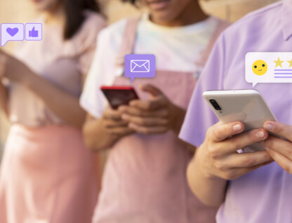 Três jovens, vestidos em tons de rosa e roxo, com celulares nas mãos. Sobre os aparelhos estão ícones de mensagem, coração, emoji e estrelas